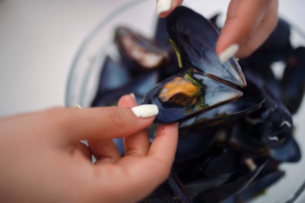 Close-up of the hands of an unrecognizable woman who eats mussels.