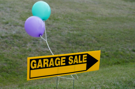 A garage sale sign into the curb of a residential neighborhood. Helium balloons are blown by the wind. Copy Space.