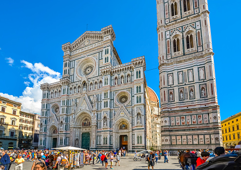 A sunny summer day in the Piazza del Duomo, with the Santa Maria Del Fiore cathedral and Giotto's Bell Tower in view as tourists enjoy the historic pedestrian zone of Florence, Italy.