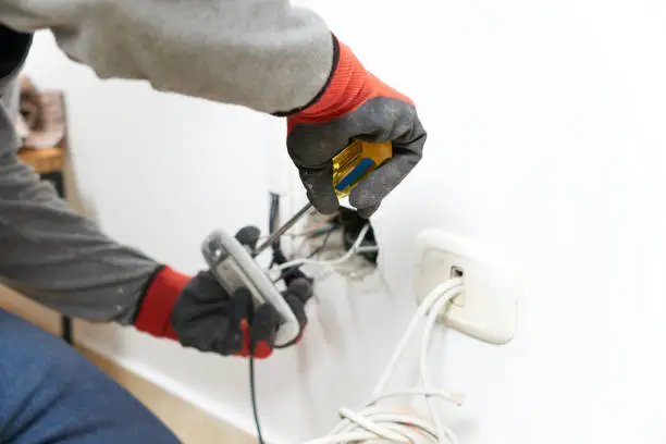 Close-up of a male electrician dismantling an electrical outlet with a screwdriver to fix it in a room