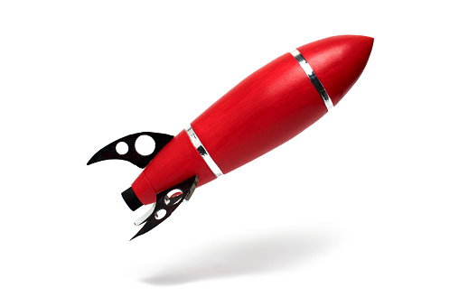 Close up of red kids baby toy rocket above the ground with silver stripes and black supports and visible shadow on white background