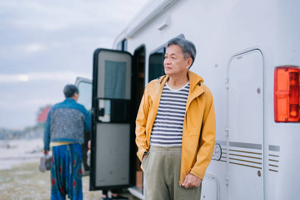 homme âgé chinois asiatique avec coupe-vent regardant ailleurs devant un camping-car - motor home mobile home camping senior adult photos et images de collection