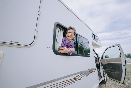 happy Asian chinese senior woman looking away from motor home window