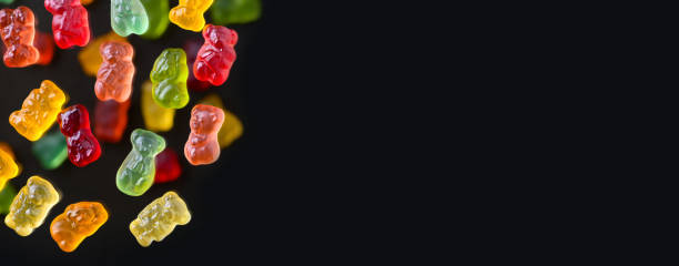 istock Multicolored flying gummy bears on a black background, flat lay. Banner 1393061696