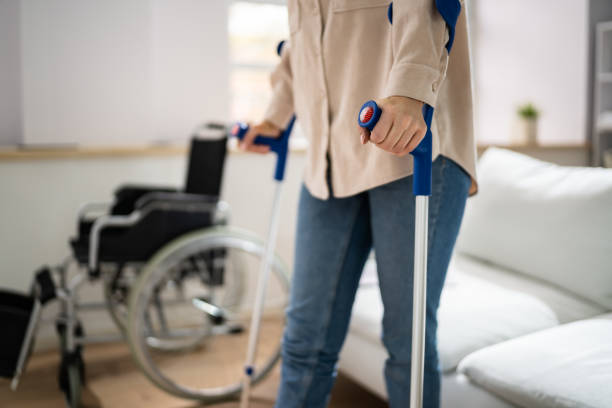 jambe blessée à l’aide de béquilles près d’un fauteuil roulant - crutch photos et images de collection