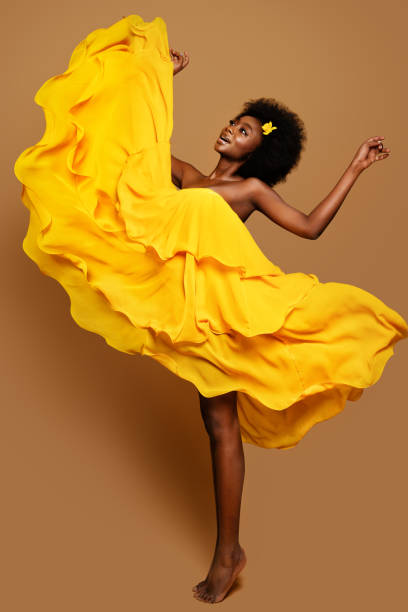 выразительная женщина танцует в желтом летающем платье. счастливая темнокожая танцовщица в размахивающем тканевом платье. модель с черным - human head black women dress стоковые фото и изображения