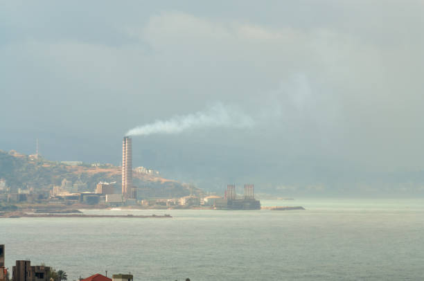 Old smokestacks and warehouses reflect on calm water in a monochromatic scene