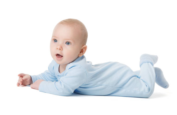 süßes baby liegt auf dem bauch über weißem hintergrund in baumwolle babys bodysuit. säugling vier monate kind in blue onesies kleidung kriechend eine seite aussehend. junge im pyjama isoliert - onesie stock-fotos und bilder