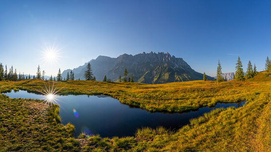 Panorama of Lake in Austrian Mountains Sun Reflecting in Water, Clear Blue Sky, Majestic Mountain Range in Backgound