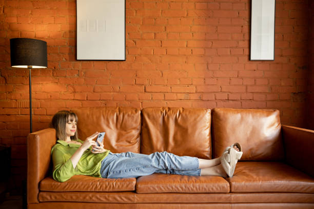 istock Woman using phone while relaxing on a leather couch at home 1393077184