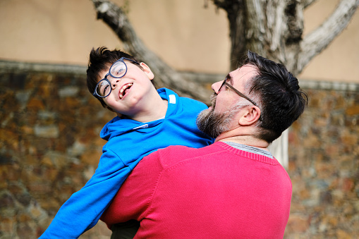 Loving father holding and playing with his disabled son while enjoying time together outdoors. Disabled people and parenthood concept.