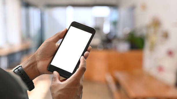 istock Close up view man hands using smartphone with blurred coffee shop background. Empty screen for graphic display montage. 1393088645