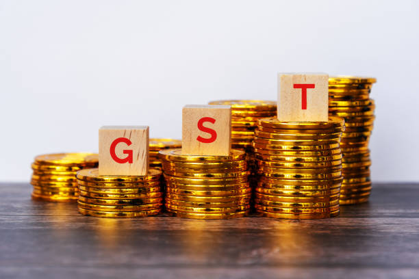 GST acronym Government Service Tax on wood block with stack of gold coins stock photo