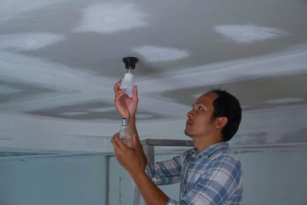 istock asian men changing a lightbulb from orange incandescent lightbulb to LED lightbulb. In house being built. 1393093365
