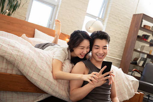 Young lovers lying on the bed to play mobile phone