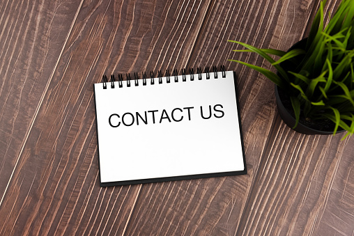 Contact us text on note pad on top of office desk with potted plant