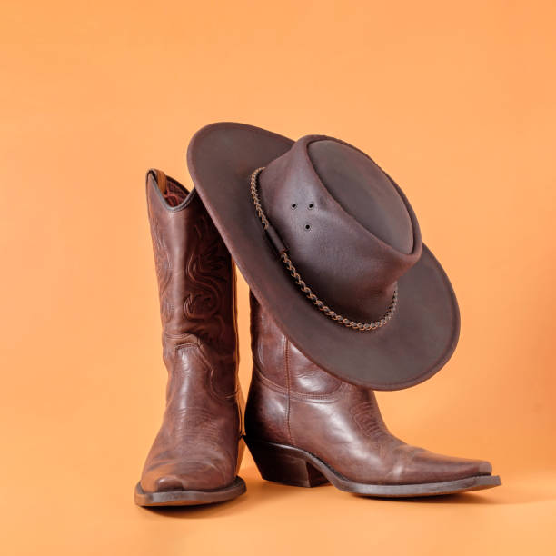 istock Two elegant classic boots and a leather cowboy stetson hat on an orange clay background. Ranger cowboy concept on a ranch in america usa texas. 1393104458