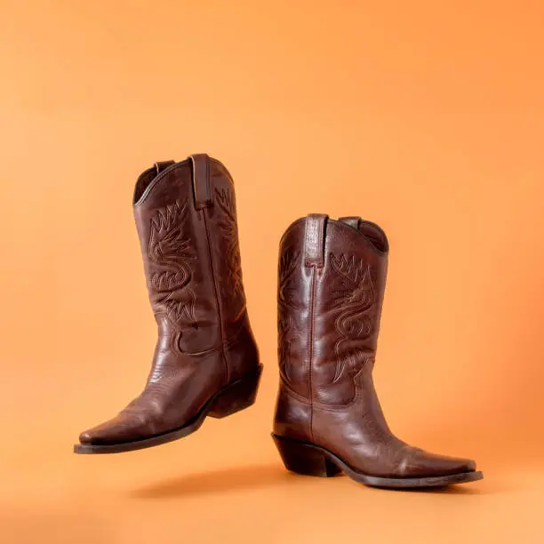 Photo of Two elegant classic cowboy boots on an orange clay background. Ranger cowboy concept on a ranch in america usa texas.
