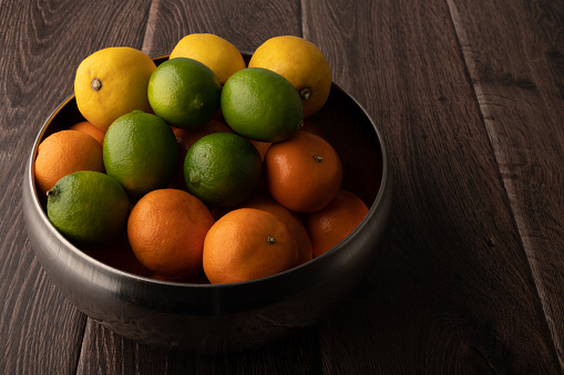 Oranges, lemons, and limes in a bowl on a wooden background