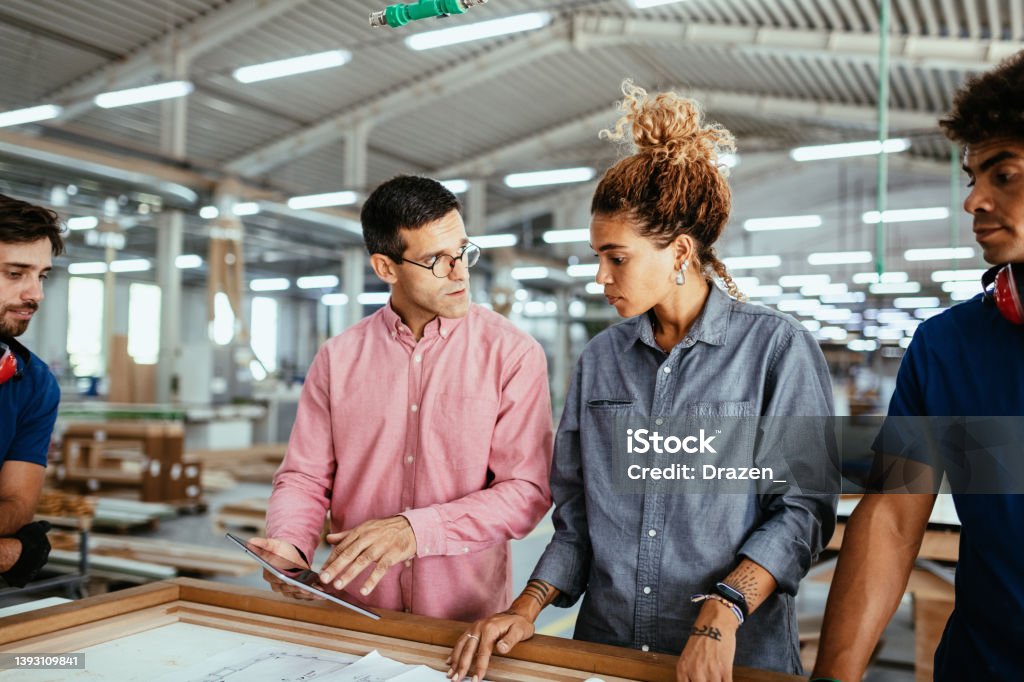 Architects, engineers and blue collar staff working together in modern factory Engineers, architects and blue collar workers in protective clothing working in factory with modern machinery Business Stock Photo