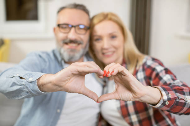 istock Married couple forming heart with their fingers on sofa 1393112914
