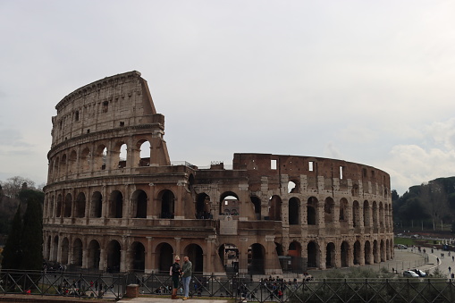 Rome, Italy - February 05, 2022: Panoramic view around the Colosseum in city of Rome, Italy. Cold and gray sky in the background. Macro photography of the green parks with the old buildings.
