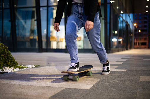 Young casually clothed hipster woman riding skateboard late night on the city street