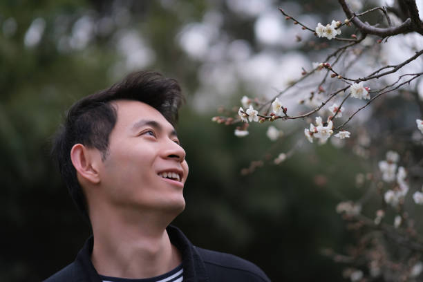 close up smiling Asian young man enjoy plum blossom flower. Handsome man look at plum blossom