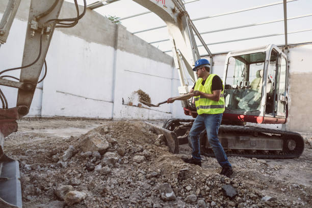 Construction worker with a shovel moves the sand so that it is less compact and looser and make the mixture in the concrete mixer