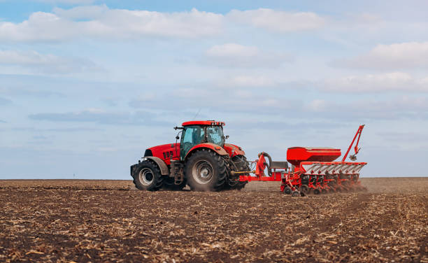 istock Spring sowing season. Farmer with a tractor sows corn seeds on his field. Planting corn with trailed planter. Farming seeding. The concept of agriculture and agricultural machinery. 1393131877