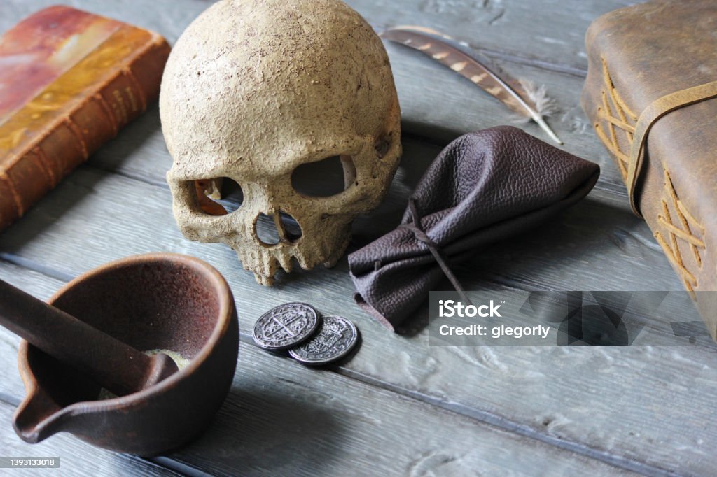 Ancient Assassin Some coins on a table with skull and books. Mystery Stock Photo