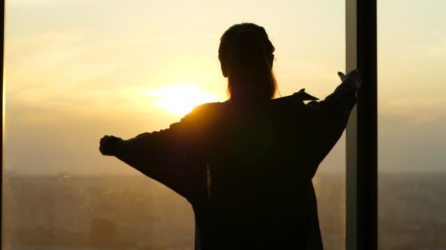 Woman puts on a light shirt, silhouette shot against the sunset