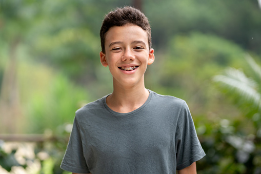 Portrait of a young teenage boy with braces laughing while standing alone outside in summer