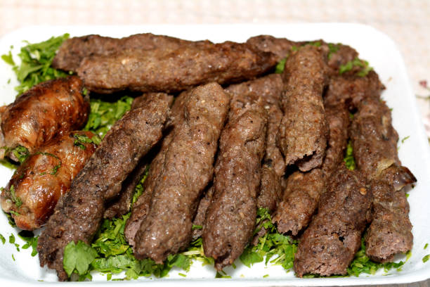 cuisine arabe nourriture traditionnelle bœuf kofta, kebab et tarb kofta qui est de la viande hachée enveloppée dans de la graisse d’agneau charbon de bois grillé et servi sur une couche de persil vert - lamb kebab kofta ground photos et images de collection