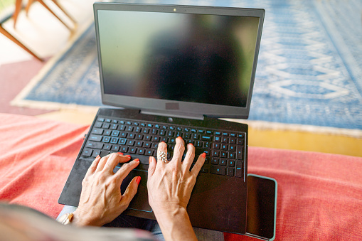 Close-up of a mature woman working on a laptop with a blank screen while sitting on a patio