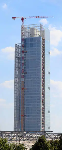 tall modern skyscraper under construction with the gigantic crane of the construction site with windows