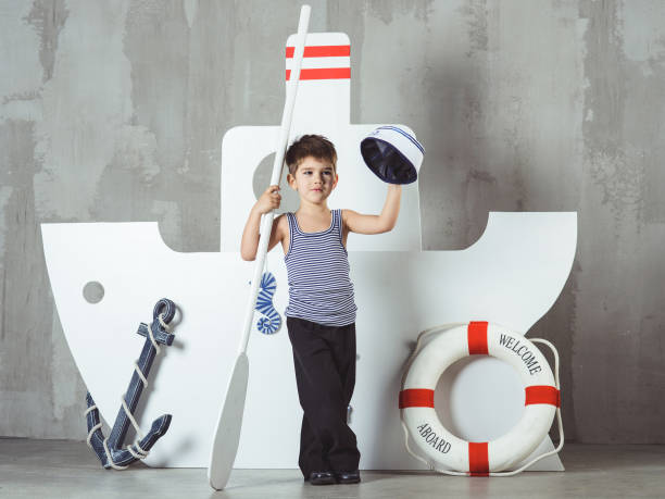A cute elementary age boy is spends time waiting for Christmas at a room decorated at Christmas. He is standing, holding the gift box, smiling and dreaming with closed eyes. Studio shooting