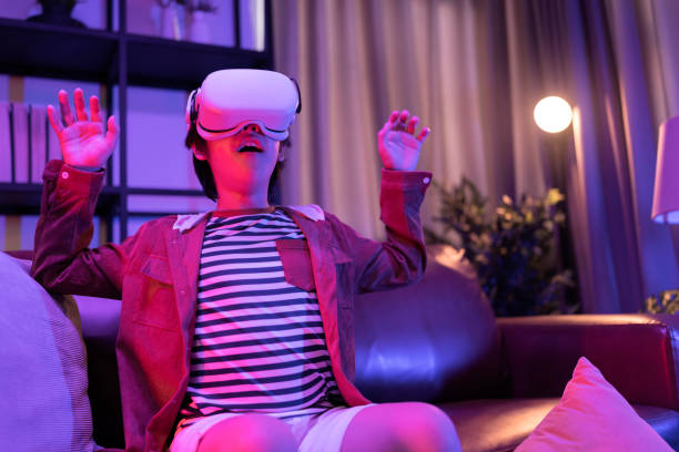 Asian child boy wear VR or virtual reality glasses,headsets standing and playing a video game at living room in front of TV at home in quarantine period technology and innovation concept neon light night lifestyle niño asiático usa gafas de realidad virtual o realidad virtual, auriculares de pie y jugando un videojuego en la sala de estar frente al televisor en casa en el período de cuarentena tecnología y concepto de innovación neón luz estilo de vida nocturn