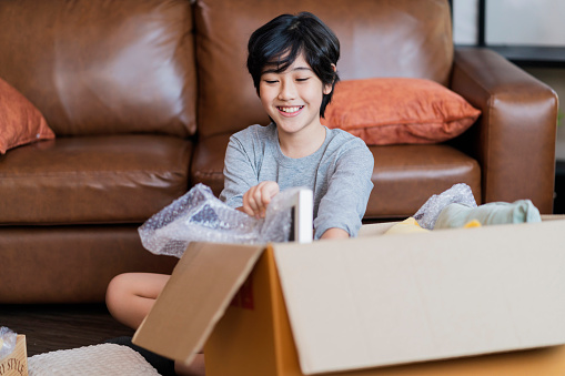 Portrait of happy Asian child male unpacking cardbox moving to new house with cardboard boxes.asian child teen smiling with confident and peaceful home moving ideas concept