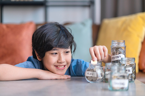 Asian child teen male hand Saving Coins In Money Jar money management education at home,smiling asian boy happiness and proud to collecting money home financial concept