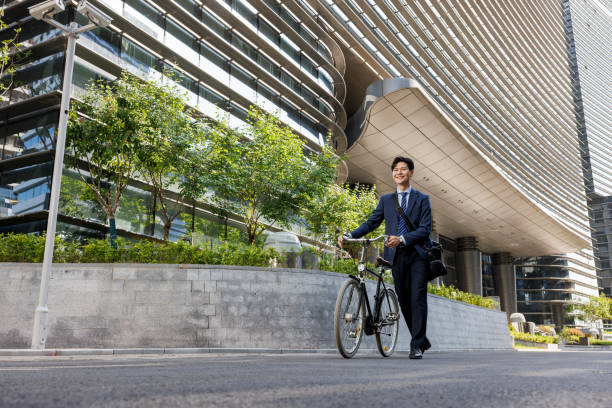Young and fashionable Asian business men, wearing gray suits. Riding a bike on the way to work. The scene is a business district in the city. The location is Zhengzhou, China.