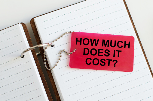 How much does it cost. business concept. Red card text on the background of an open notepad on the table