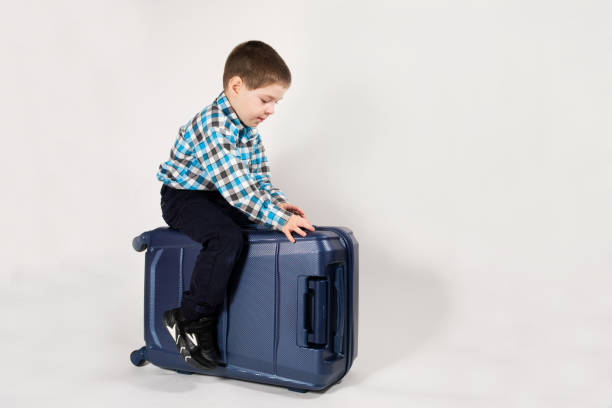 istock A 4-year-old boy sits on a blue travel suitcase on a white background with space for text. 1393154504