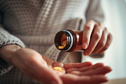 Close up photo of woman pouring pills from a pill bottle into hand.