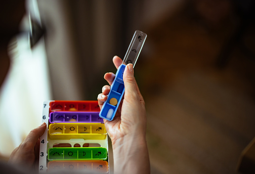 Close up photo of woman hands taking her daily vitamins and supplements from pill box.