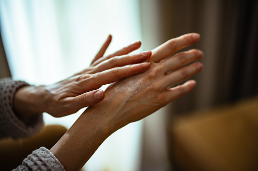 Close up photo of woman moisturizing her hands at home.