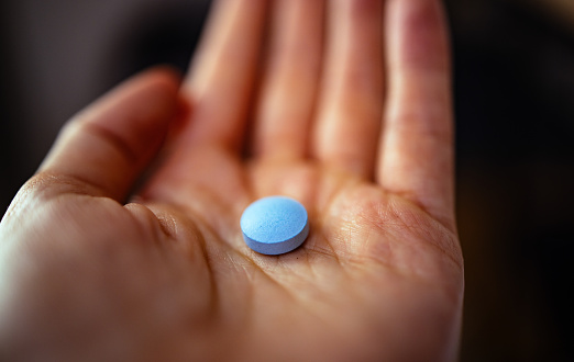 Close up photo of woman's hand holding blue pill.