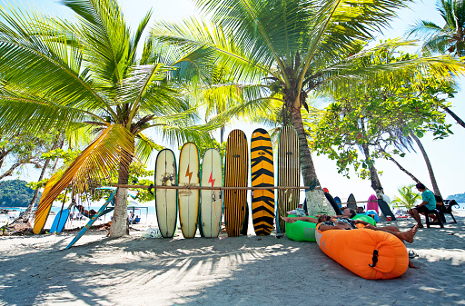 Traders rest in front of their Surf Board selection for hire, Manuel Antonio Beach, Costa Rica. Costa Rica is the central American country north of Panama that is renowned for its tropical birdlife, exotic wildlife and adventure pursuits such as whitewater rafting, parasailing and ziplining