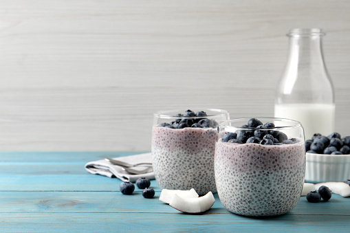 Delicious chia pudding with blueberries on light blue wooden table, space for text