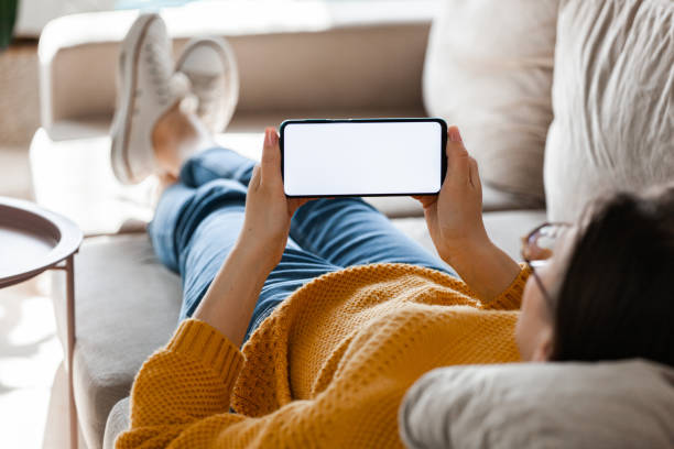 istock Young woman hold mobile phone screen mockup in hands, lying on the sofa 1393166092